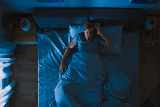 אדם שוכב במיטה בפאניקה אחרי שהתעורר בגלל חלום מעורר חרדה